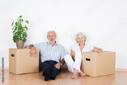 senioren-paar sitzt lächelnd zwischen umzugskartons