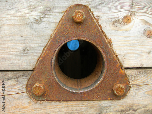 Triangular rusty metal spare part fastened at a wooden surface
