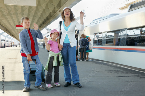 Mother with two kids and luggage stands on platform