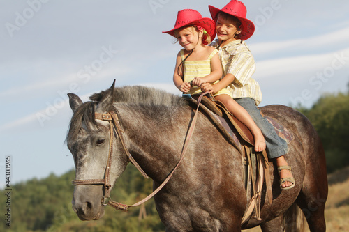 two happy children in cowboy hats riding horse on natural backgr