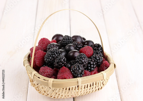 Ripe raspberries and brambles in basket on wooden table