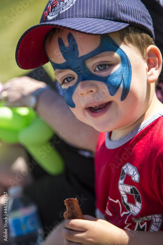 young boy with blue face paint eating a hot dog