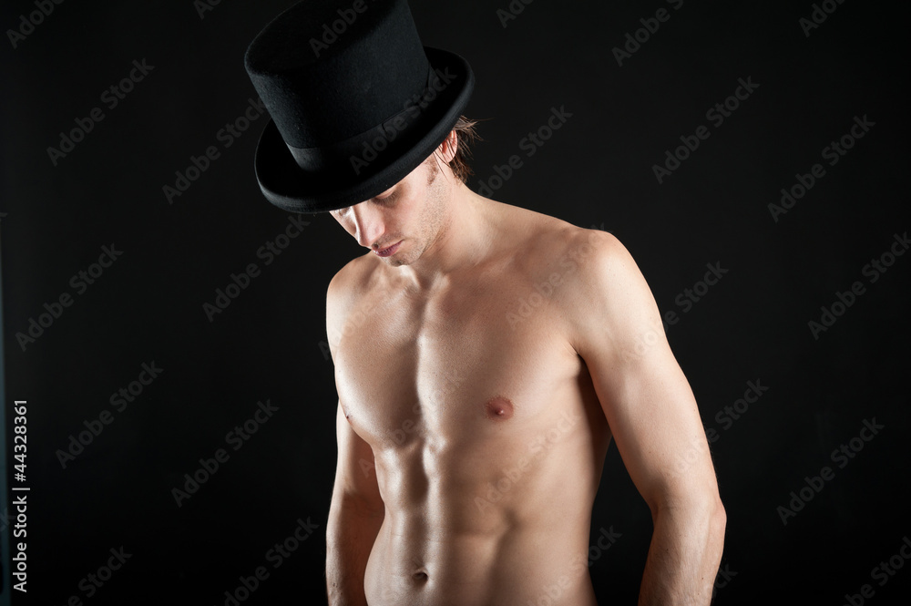 Young man shirtless with cylinder against black background.