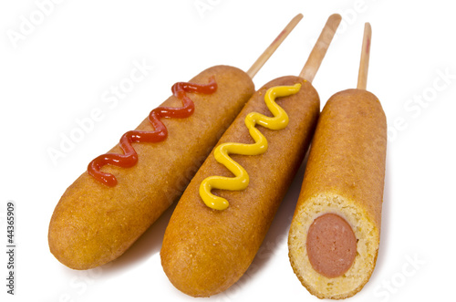 Photography Three corn dogs arranged on a white background, two topped with mustard and ketchup