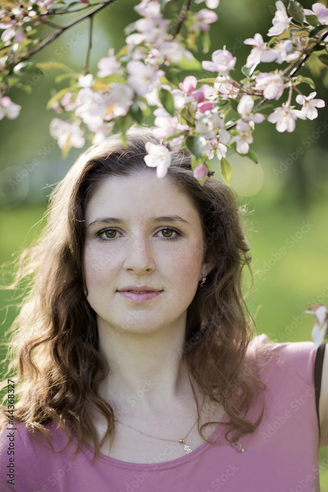 Fototapeta premium Portrait of the young woman against a blossoming apple-tree