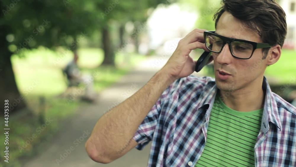 Young man talking on cellphone in the park, steadicam shot Young man talking on cellphone in the park, steadicam shot