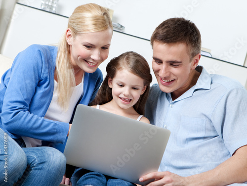 Happy family of three sit on the sofa with personal computer