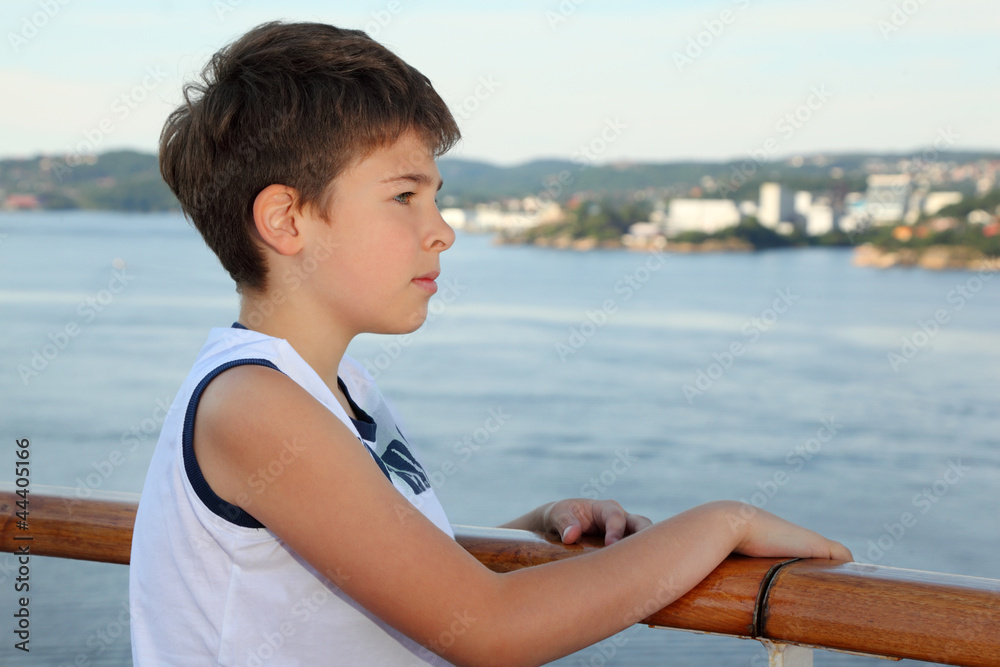Thoughtful boy stands on board of ship and looks at landscape