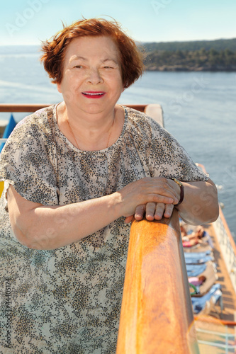 Happy elderly woman stands at board of ship and looks into dista photo