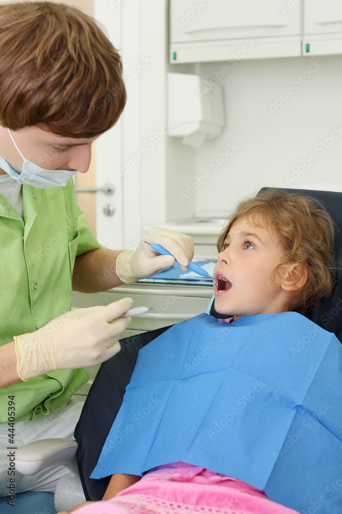 Fototapeta premium Dentist looks at teeth of little girl in dental clinic.