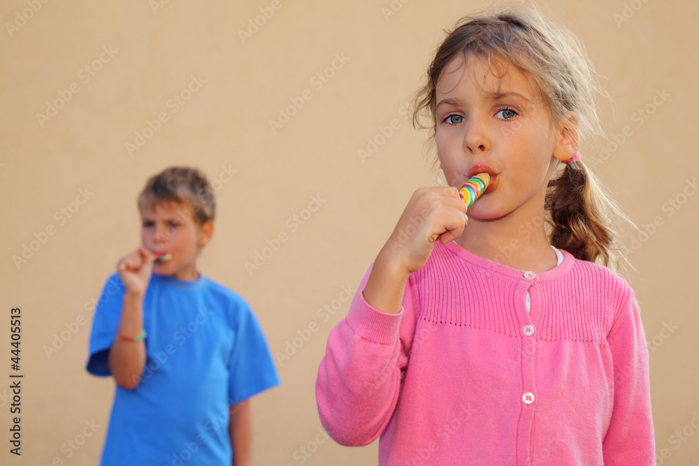 Girl and boy suck multicolored candies. Sister looks at camera Girl and boy suck multicolored candies. Sister looks at camera