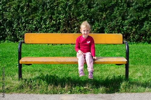 Little girl sitting on the bench in the park photo