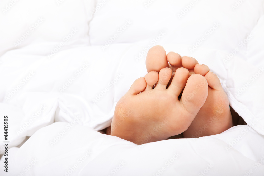 Weibliche kleine Füße unter der Bettdecke Weibliche kleine Füße unter der Bettdecke