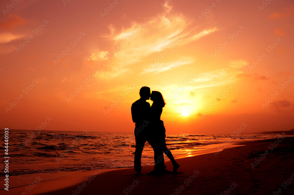 an amorous couple are kissing at sundown