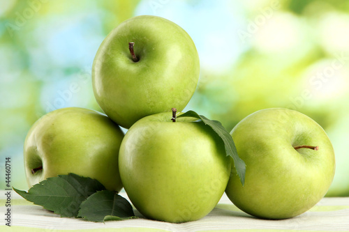 Ripe green apples with leaves, on table, on green background