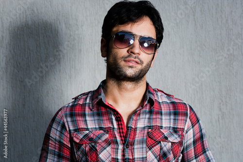 close up of a man wearing sunglasses against  grey wall