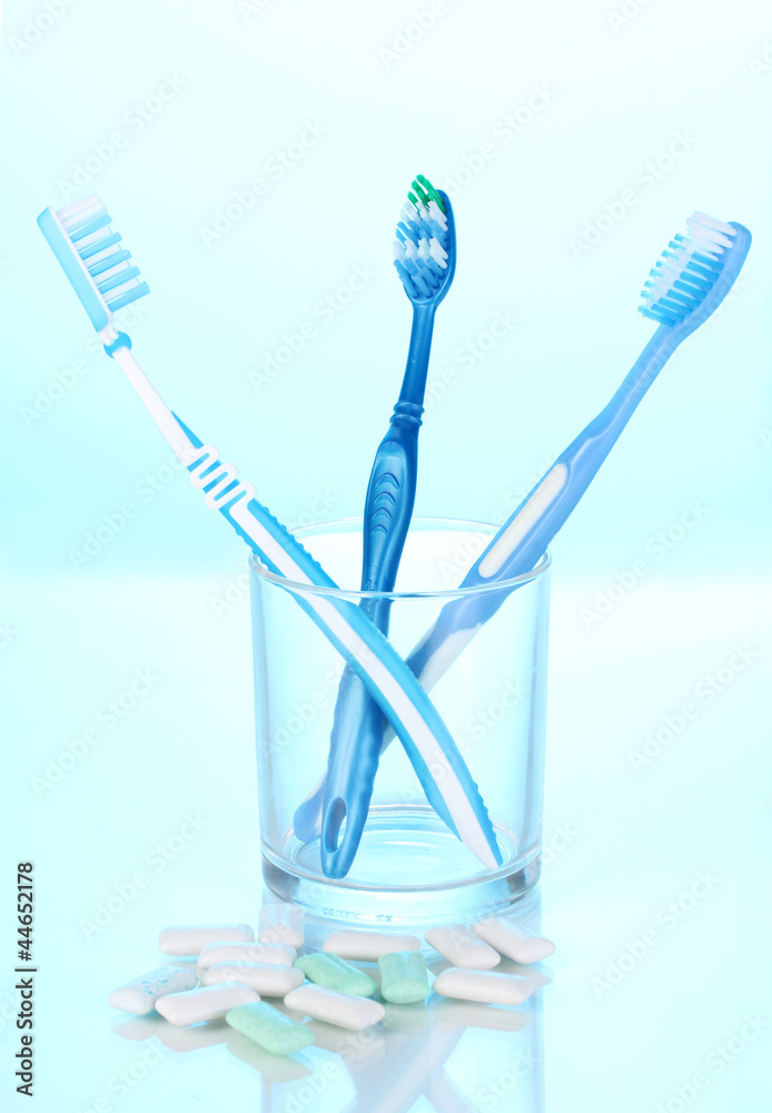 Toothbrush in glass and chewing gum on blue background Toothbrush in glass and chewing gum on blue background