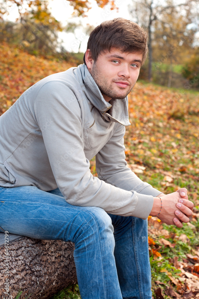 Outdoors portrait of happy young man sitting in autumn park Outdoors portrait of happy young man sitting in autumn park