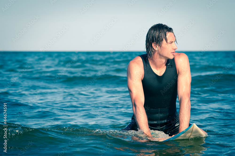 Young surf man relaxing in the water with a surfboard.