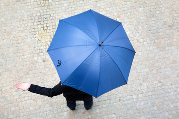 Business man hidden under umbrella and checking if it's raining