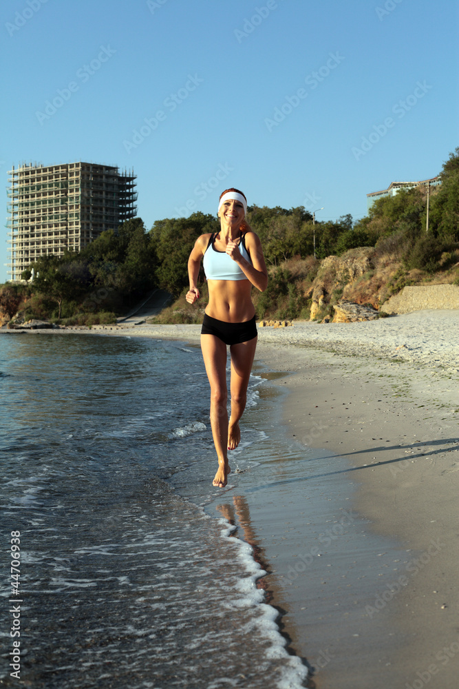 Beautiful young sport woman running on beach on sunny summer day
