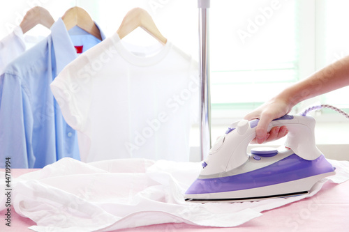 Woman hand ironing a shirt, on cloth background