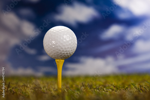 Golf ball on green grass over a blue sky 