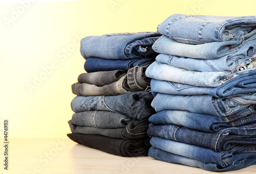 Many jeans stacked in a piles on yellow background