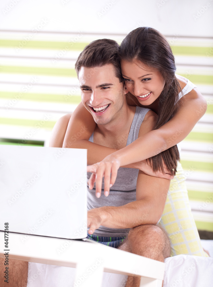 © luckybusiness - Young couple in bedroom using laptop