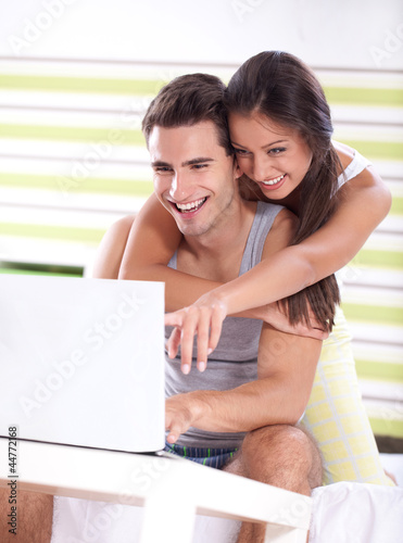 Young couple in bedroom using laptop