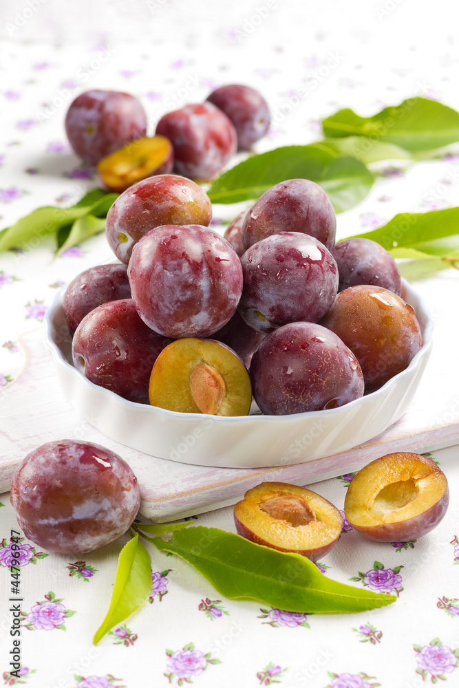 Fresh wet plums with leaves in the bowl on the vintage board Fresh wet plums with leaves in the bowl on the vintage board