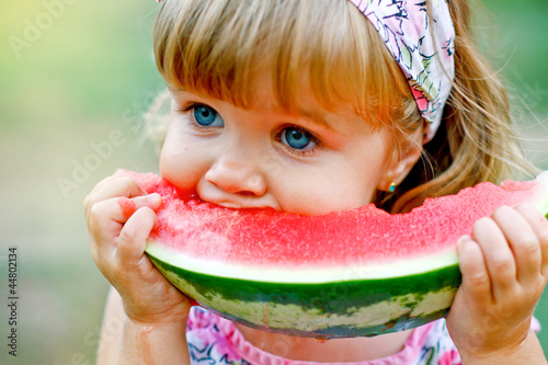 Adorable little girl eats a slice of watermelon outdoors