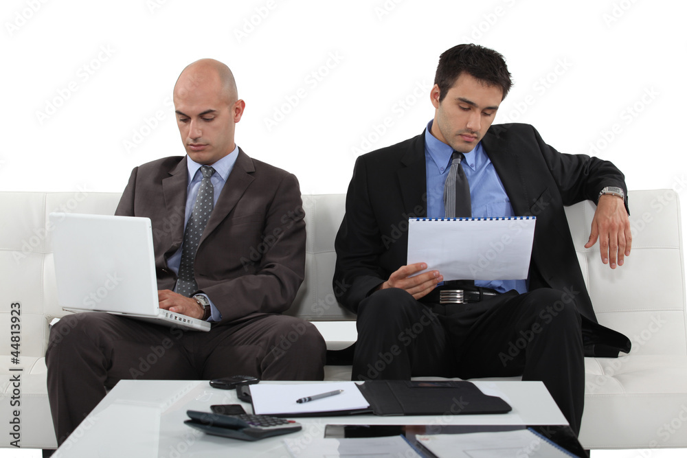 Two determined businessmen sat waiting for presentation Two determined businessmen sat waiting for presentation