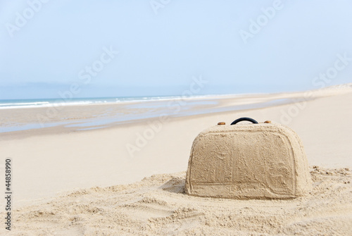 Suitcase made out of sand on beach
