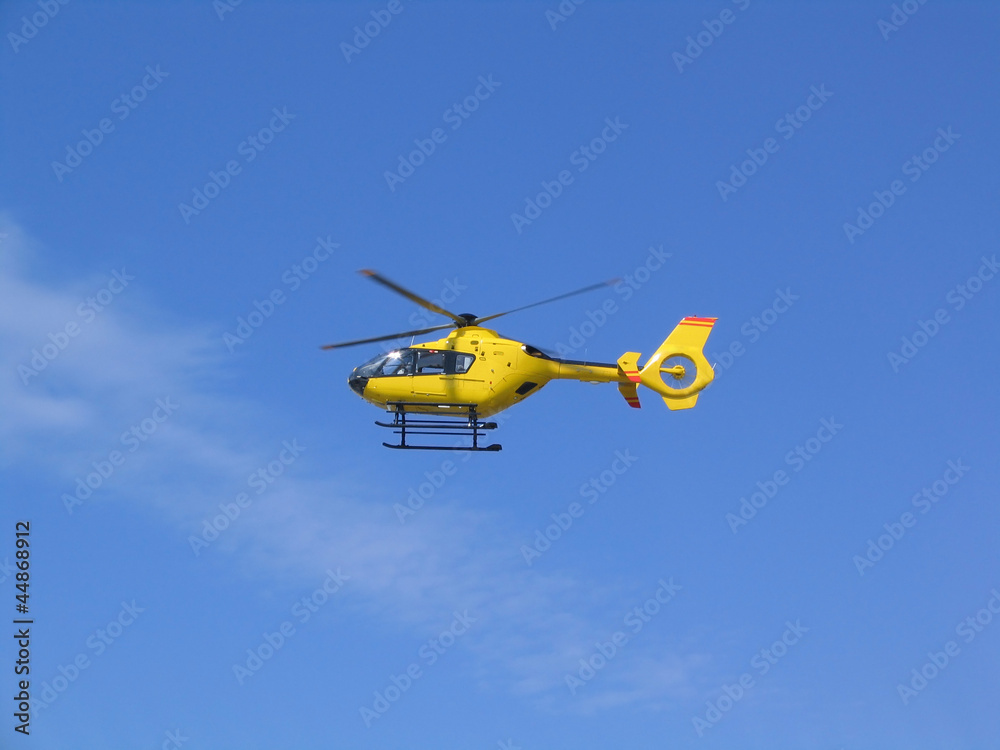 Fototapeta premium Small yellow helicopter in the air, blue sky in background
