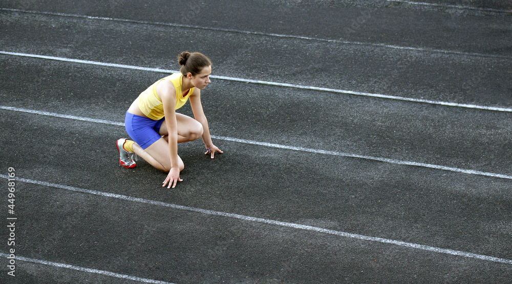 Fototapeta premium Athletic teenage girl in start position on track .