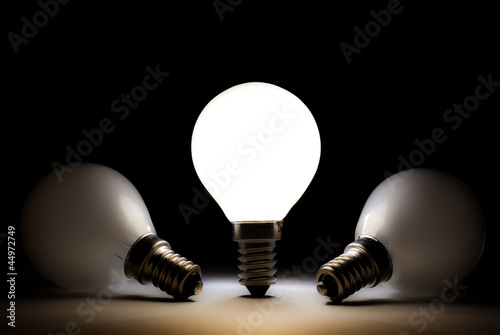 One light bulb shining in a dark space with other dead bulbs