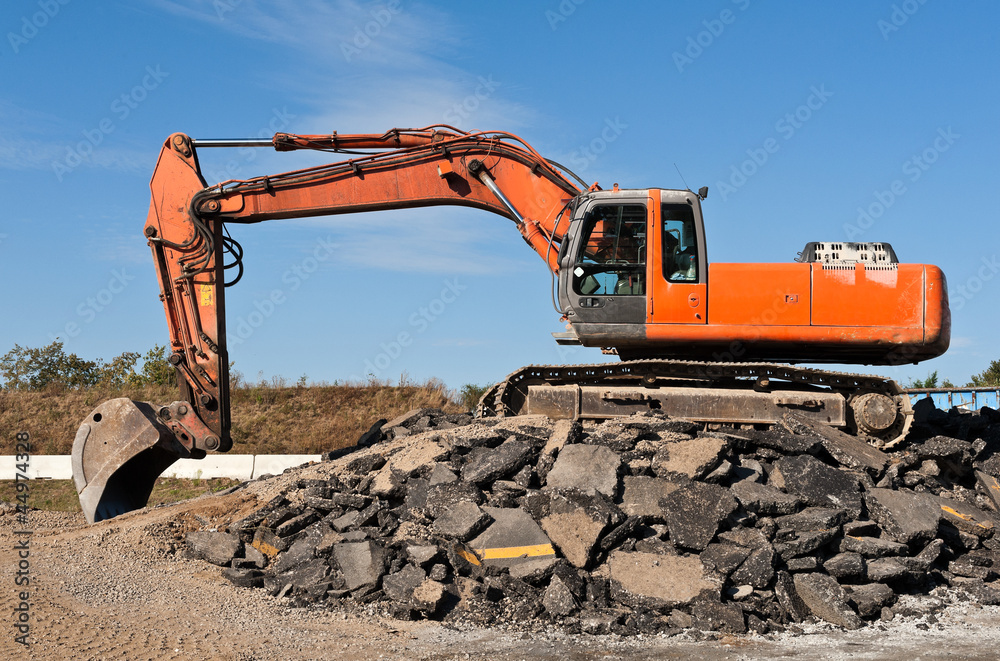 Oranger Bagger auf einem Haufen Asphaltbruch Oranger Bagger auf einem Haufen Asphaltbruch