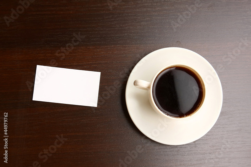 A cup of coffee and a note card on a wooden desk from above