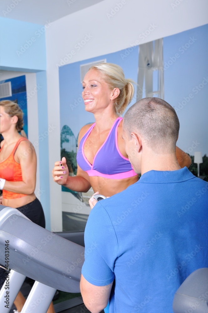 Two women in gym exercising with personal fitness trainer Two women in gym exercising with personal fitness trainer