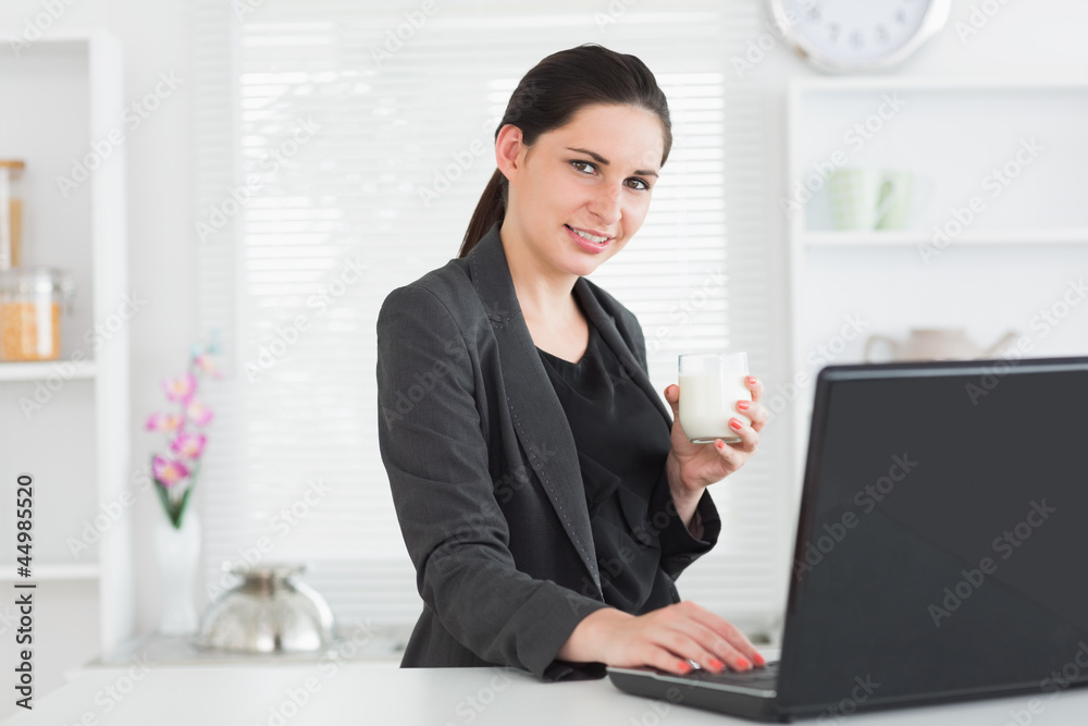 Smiling woman in front of laptop with glass of milk Smiling woman in front of laptop with glass of milk