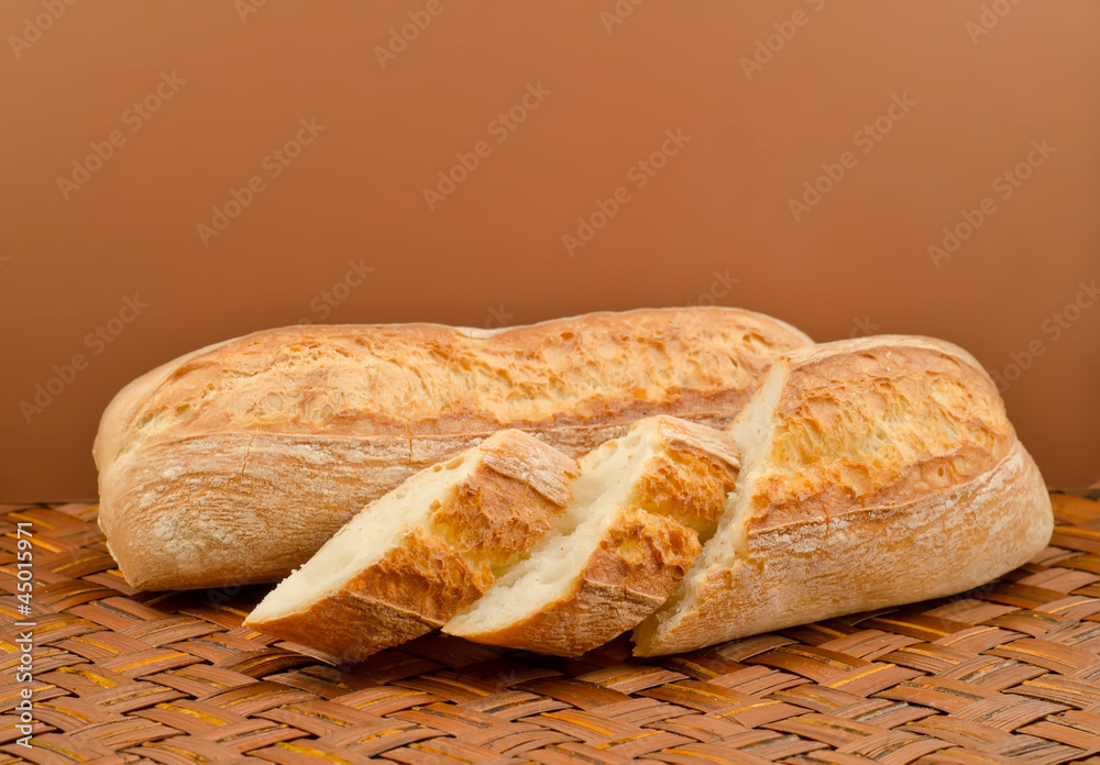 two baguette bread on a wicker table cloth on a brown background