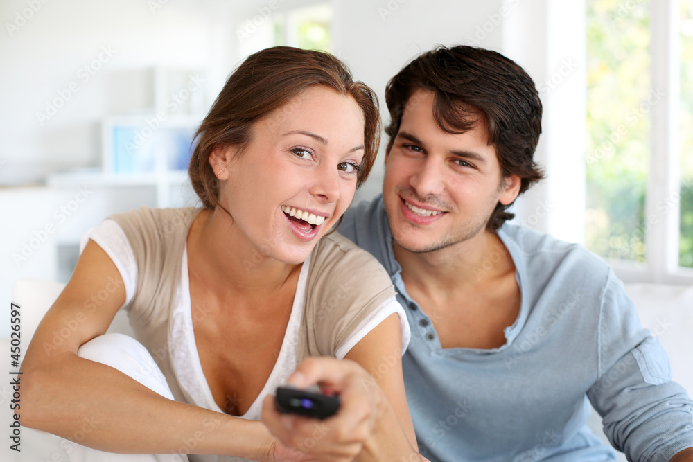 Fototapeta premium Couple sitting in sofa with remote control in hands