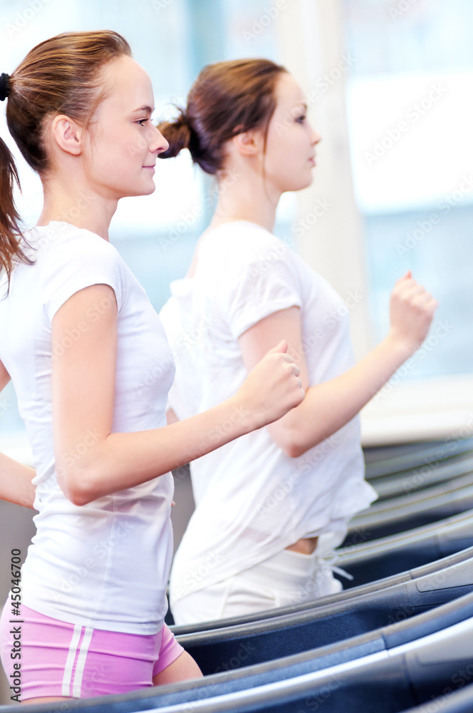 Fototapeta premium Two young sporty women run on machine