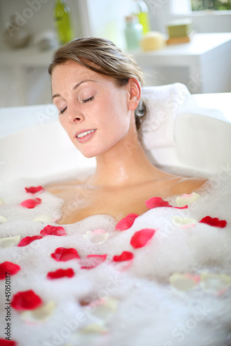 Beautiful woman relaxing in bath with rose petals
