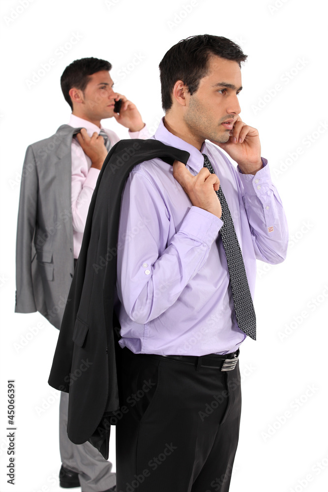 Two businessmen stood taking on their mobile telephones Two businessmen stood taking on their mobile telephones