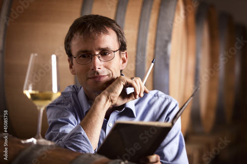 Pleased vintner looking at a glass of white wine in cellar.