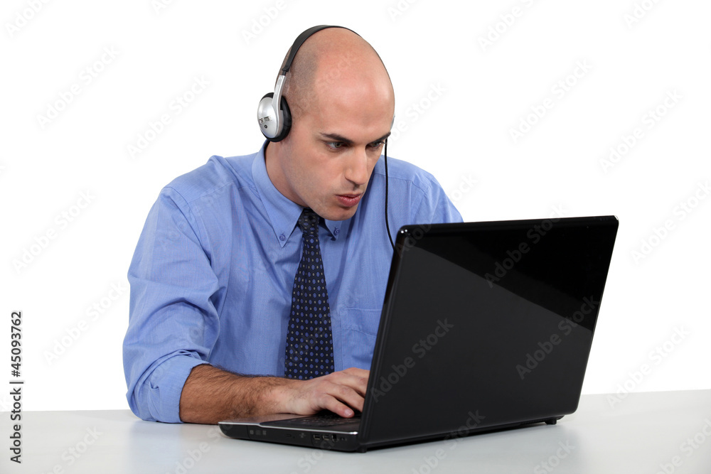 Businessman wearing headphones typing on laptop