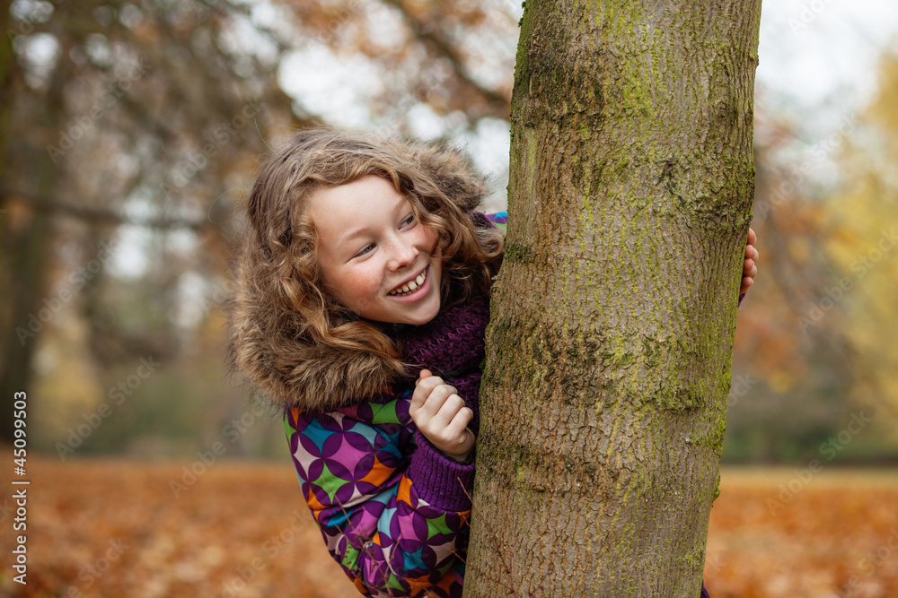 Smiling girl hiding behind a tree Smiling girl hiding behind a tree