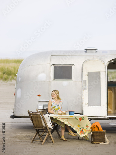 woman sitting at a table on the beach outside her airstream classic trailer